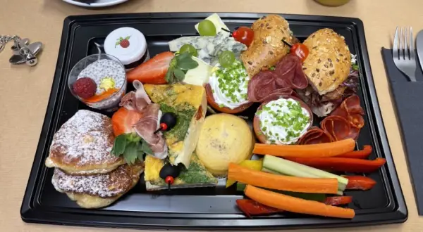 Taca ze śniadaniem kontynentalnym: naleśniki, omlet, sery, wędliny, owoce, warzywa i napój.