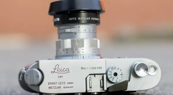 A Leica M4 camera with a Leitz Wetzlar lens. The camera body shows "Leica M4" and "Ernst Leitz GmbH Wetzlar Germany." The lens has aperture markings and a focus ring. The framelines are not visible in this shot.