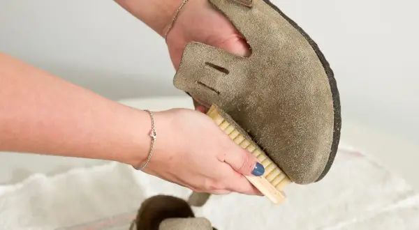 Hände reinigen Wildlederschuh mit Bürste. So lassen sich hartnäckige blutflecken aus leder entfernen und das Material wird wieder wie neu.