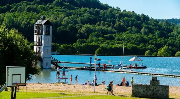 Słoneczny dzień na kąpielisku Stara Morawa. Ludzie odpoczywają na plaży, pływają i korzystają z uroków jeziora. W tle zielone wzgórza.