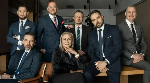Grupa siedmiu profesjonalistów w garniturach, w tym jedna kobieta, pozuje do zdjęcia.