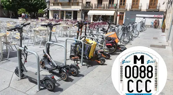 Patinetes eléctricos y bicicletas aparcados en una plaza. Se ve una pegatina de la DGT con la matricula CD.
