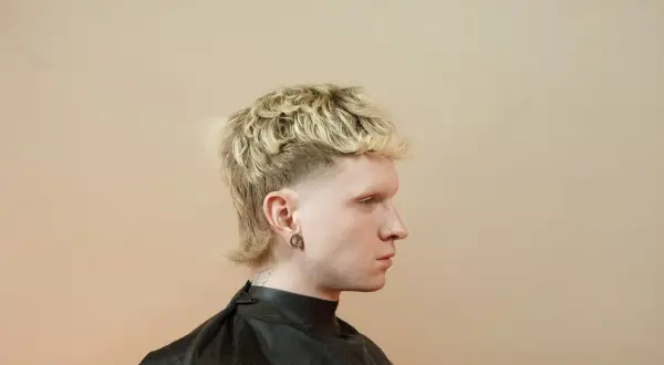 Młody mężczyzna z blond, kręconymi włosami i charakterystyczną fryzurą mullet.