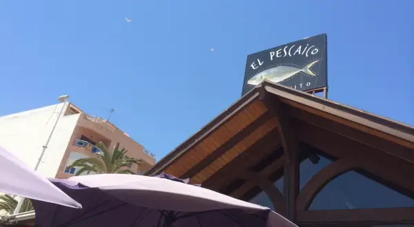Un cartel de "El Pescaito" con un dibujo de pez, bajo un cielo azul con gaviotas.