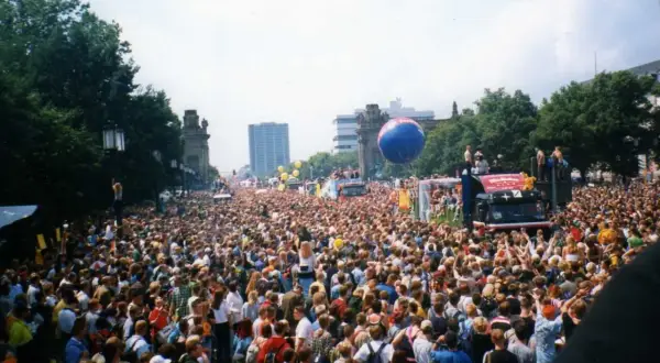 Tłum ludzi na ulicy podczas Love Parade, z wielkim niebieskim balonem i ciężarówką z platformą.