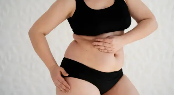 Une femme en sous-vêtements noirs touche son ventre, peut-être à cause d'un **gonflé ventre hormonal**.