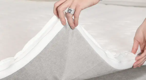 Hände ziehen den Reißverschluss eines Toppers ab, um die **Boxspringbett Pflege** zu erleichtern.