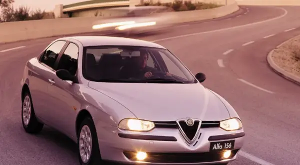 En silverfärgad Alfa Romeo 156 kör på en kurvig väg i solnedgången.