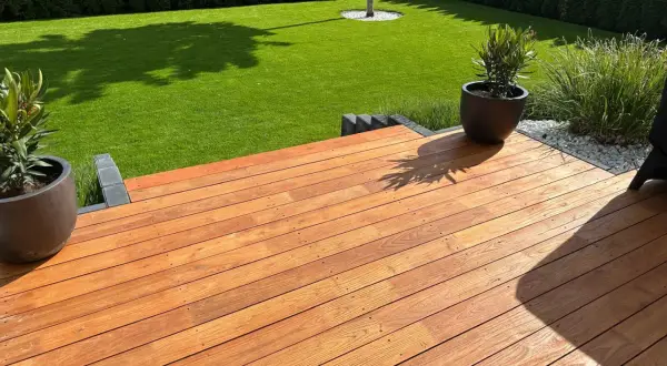 Terraza de madera de robinia con césped verde y plantas en macetas.