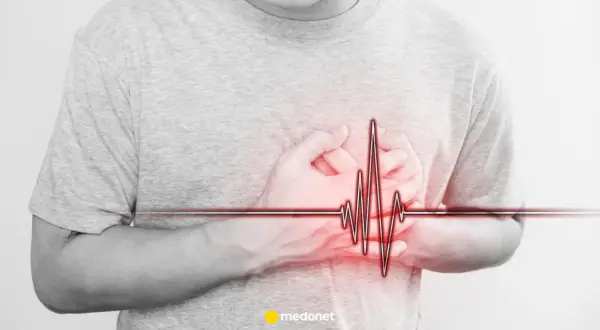 Osoba trzyma się za serce, na którym widnieje wykres EKG. Może to symbolizować problemy z sercem, jak np. arytmia, lub po prostu stres.