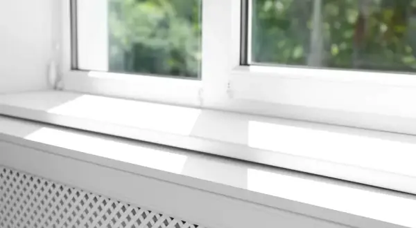 Biały parapet na równo ze ścianą, z widocznym kratkowanym grzejnikiem pod oknem.