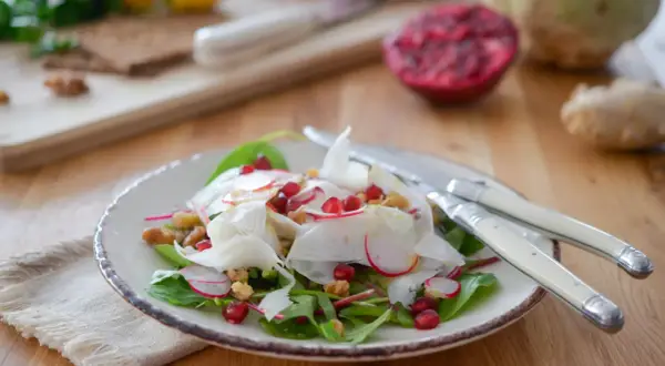 Salade croquante de céleri rave, radis, grenade et noix, garnie de feuilles vertes. Un délice frais et coloré.