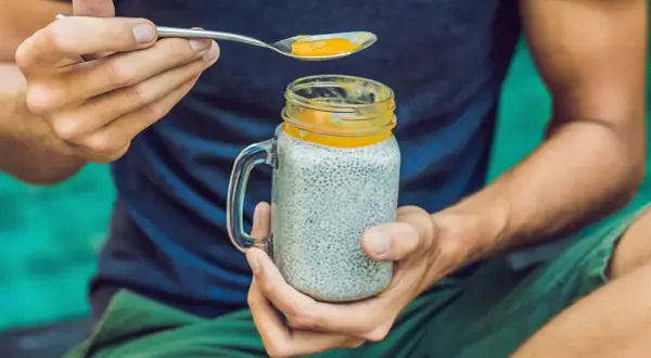Mann hält ein Glas Chia-Pudding mit Mango-Topping. Die Frage "wieviel chiasamen pro tag" wird durch die gesunde Mahlzeit beantwortet.