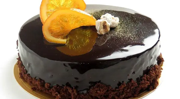 Torta lucida al cioccolato con fette d'arancia candita e nocciole. Un delizioso mousse cioccolato e arancia che invita a un assaggio.