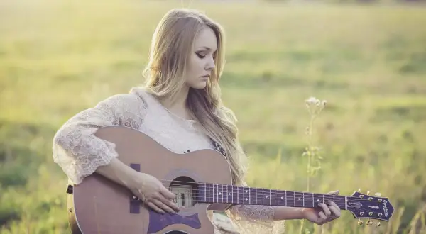 Dziewczyna gra na gitarze w plenerze. Czy wiesz, że gitara akustyczna ma swoje ciekawostki o muzyce?