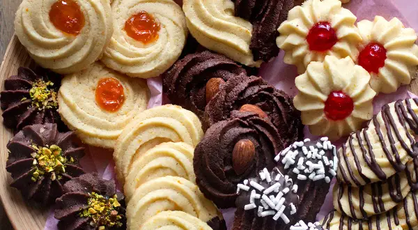 Variazioni di frolla montata: biscotti al cacao con mandorle e pistacchi, frollini con marmellata d'arancia e ciliegia, e decorati con cioccolato.