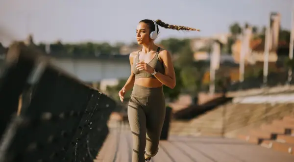 Donna con cuffie corre 10 km su un ponte, concentrata e determinata, con la treccia che ondeggia al vento.