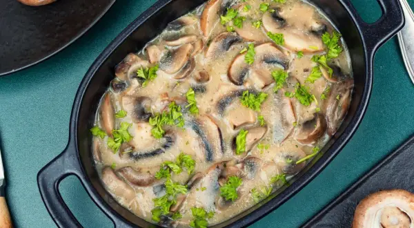 Aksamitny sos pieczarkowy z mascarpone, udekorowany natką pietruszki, w czarnej miseczce.