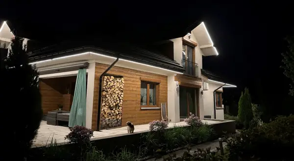 Nowoczesna iluminacja podkreśla architekturę domu i ogród. Wzdłuż dachu biegną świetlne linie, tworząc efektowną **modernizację oświetlenia**.