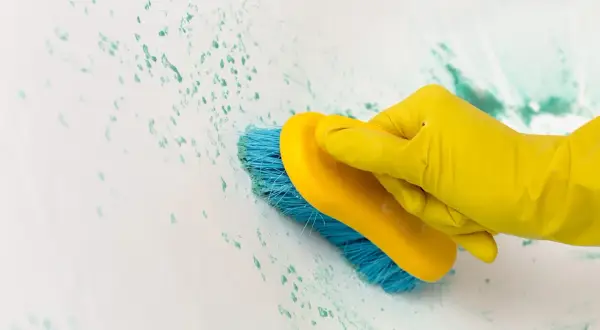 Main jaune, brosse bleue frottant une tache sur carrelage qui ne part pas.