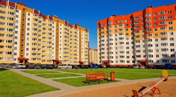 Nowe bloki z wielkiej płyty w kolorach żółtym i pomarańczowym, z parkingiem i placem zabaw.