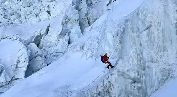 Bergsteiger seilt sich im Khumbu Icefall ab, umgeben von zerklüftetem Eis und tiefen Gletscherspalten.