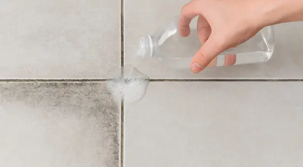 Main d'une personne versant un produit nettoyant sur des joints de carrelage très encrassés pour les faire mousser.