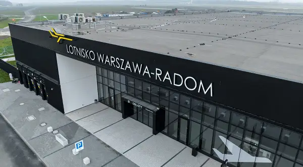 Nowoczesny budynek lotniska Warszawa-Radom z napisem "ODLOTY" i symbolem samolotu na szkle.