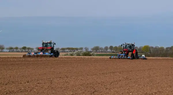 Deux tracteurs préparent le sol pour la culture du lin. Le champ est labouré, prêt pour les semis.