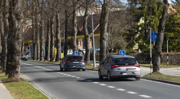 Dwa samochody z literą "L" na dachu, przygotowujące się do egzaminu praktycznego na prawo jazdy. Zastanawiasz się, ile kosztuje egzamin praktyczny na prawo jazdy?