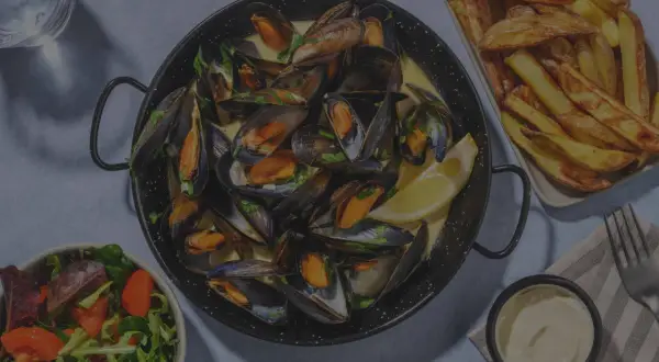 Un plat de moules frites, accompagné d'une salade fraîche et d'une sauce crémeuse. Un délice pour les amateurs de fruits de mer.