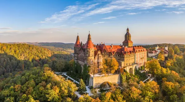Zamek Książ w malowniczej kotlinie kłodzkiej, otoczony jesiennymi barwami lasów, prezentuje się majestatycznie na tle błękitnego nieba.
