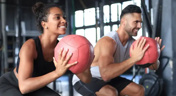 Coppia sorridente si allena in palestra con palle mediche. Non preoccuparti se il primo mese di palestra si ingrassa, è normale!