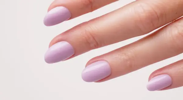 Une main aux ongles courts et arrondis, peints d'un joli violet pastel. Une idée ongle violet douce et élégante.