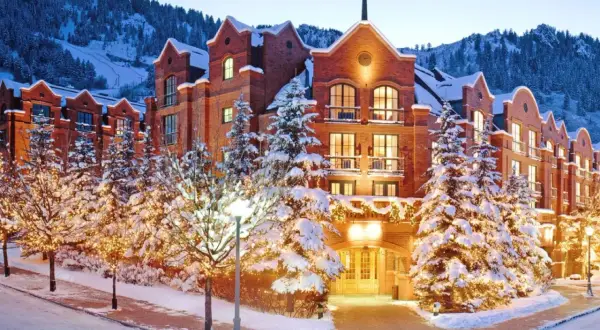 Luxuriöses Hotel im teuersten Skigebiet der Welt, umgeben von verschneiten Bäumen mit Lichterketten und Bergen im Hintergrund.
