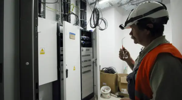 Elektryk w kasku i kamizelce odblaskowej przy skrzynce elektrycznej.