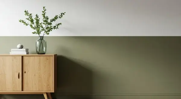 Ein Flur zweifarbig gestrichen: oben weiß, unten ein warmes Olivgrün. Ein Holzschrank mit Deko und Pflanzen.