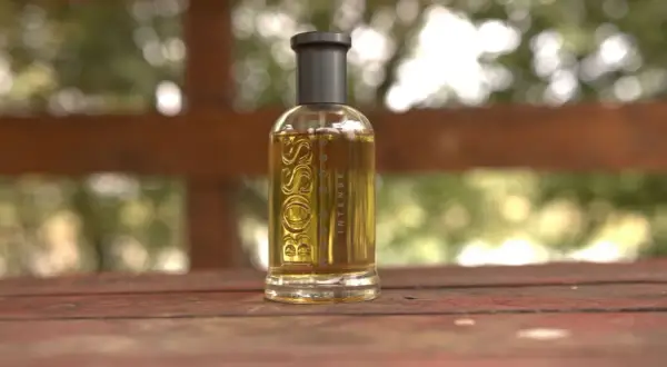 Szklana butelka perfum Boss Bottled Intense, z płynem o bursztynowym kolorze, stoi na drewnianym stole.