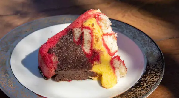 Una fetta di zuppa inglese, con pan di Spagna rosso e giallo e crema al cioccolato, su un piatto decorato.