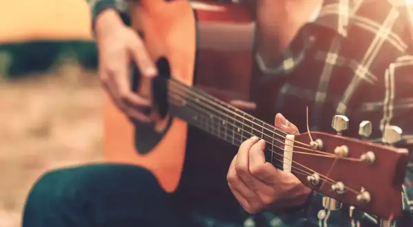 Un uomo con una camicia a quadri suona la chitarra acustica, creando una canzone per salutare colleghi.