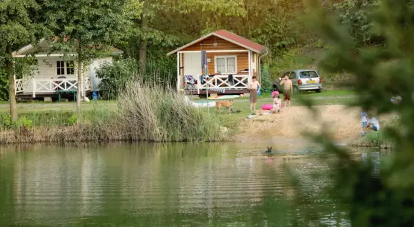 Rodzina odpoczywa nad jeziorem w **camping forteca**. Dzieci pluskają się w wodzie, a dorośli relaksują się na plaży przy domkach.