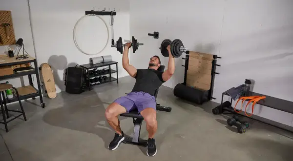 Un homme fait un exercice banc de musculation avec des haltères.
