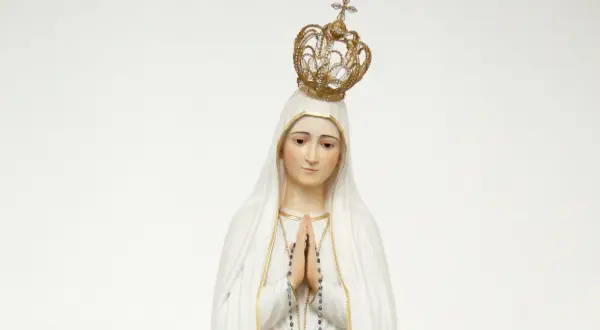 Figurka Matki Bożej Fatimskiej w białym welonie i złotej koronie, z rękami złożonymi do modlitwy.