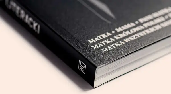 Czarny grzbiet książki z białym napisem "MATKA KRÓLOWA WSZYSTKICH SZCZĘŚLIWYCH". Ten artykuł to prawdziwe dzieło sztuki.