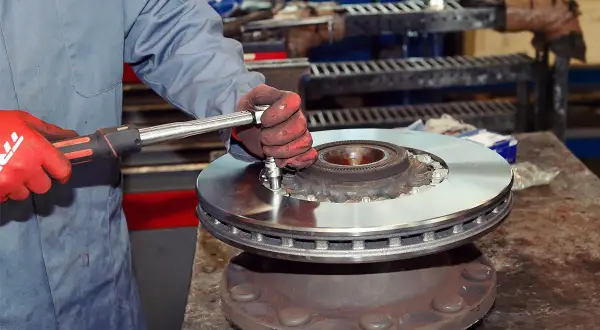 Mechanik w czerwonych rękawicach dokręca śruby podczas wymiany tarcz hamulcowych.