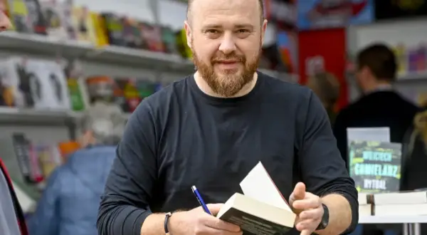 Chmielarz cykl gliwicki. Autor z książką i długopisem, w tle regały z publikacjami.