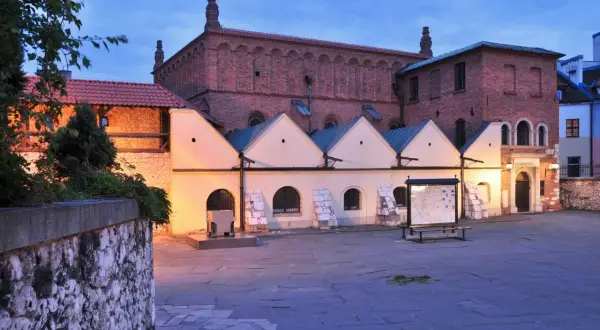 Stara synagoga w Krakowie o zmierzchu. Ceglana fasada, jasne przybudówki i kamienny dziedziniec tworzą historyczny klimat.