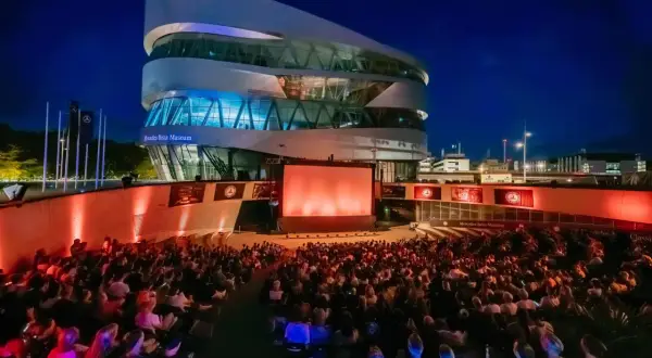 Ein großes Publikum genießt einen Filmabend beim Mercedes-Benz Museum Open Air. Die moderne Architektur des Museums bildet die beeindruckende Kulisse.