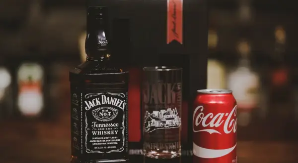 Zestaw na drinka: butelka Jack Daniel's, szklanka z logo destylarni i puszka Coca-Coli. Idealny na wieczór z klasycznym jack and coke.