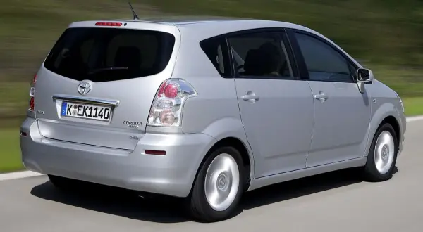 Srebrny Toyota Corolla Verso 2005 jedzie po drodze, w tle zielone wzgórza.
